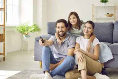 Evde televizyon izleyen mutlu bir çekirdek aile. Anne, baba ve çocuk oturma odasındaki koltuğun yanında oturuyor, gözlerini kaçırıyor, birlikte televizyon seyrediyor ve gülümsüyor.