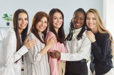 Birlikte çalışan başarılı kadın meslektaşlar, modern ışık ofisinin iç kısımlarına karşı poz veriyorlar, birbirlerine yakın duruyorlar ve mutlu bir şekilde gülümsüyorlar. Bir grup şirket çalışanı