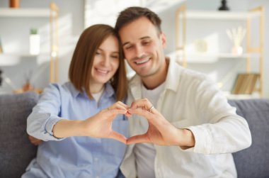 Birbirine aşık çiftler kalp çerçevesi, aşk portresi, aşık mutlu erkek ve kadın, eğleniyor, poz veriyor, gülümsüyor, birlikte tatilden zevk alıyor, birlikte tatilleri kutluyor, kanepeye yakın oturuyor. 