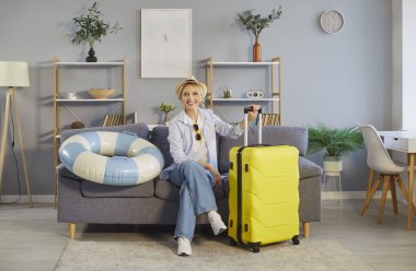 Bavullu mutlu bir kadının portresi oturma odasındaki kanepede oturur, yaz gezisine hazır tatil hazırlıkları ve ayrılmadan önce heyecana odaklanmış bir ortamda..