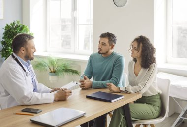 Doktor konuşuyor, toplantı yapıyor, tüp bebek kliniğindeki mutlu çift hastalara danışıyor, yardım öneriyor, tıbbi tavsiyelerde bulunuyor, profesyonel klinisyenlerle konuşuyor, karı-koca planlama, test muayenesi yapıyor.