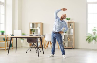 Modern ofisteki iş yerinde spor egzersizleri yapan mutlu genç bir iş adamı. Gülümseyen bir şirket çalışanı bir işe ara verirken sağlık için egzersiz yapıyor..