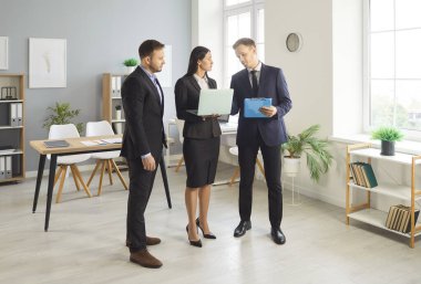 Genç iş adamları iş yerlerinde iş arkadaşlarıyla dizüstü bilgisayarlarını tutuyorlar. İş arkadaşları ve şirket çalışanları bir toplantı sırasında yeni bir proje veya girişimi tartışıyor, şirketi analiz ediyorlar.