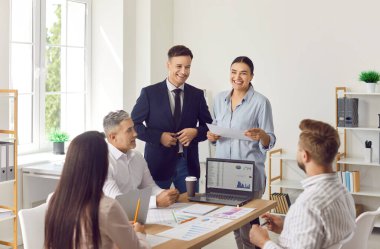 Gülümseyen iş dünyası liderleri iş arkadaşlarına sunum yapıyorlar, dizüstü bilgisayarlarında proje istatistikleri ve mali sonuçları gösteriyorlar, iş projesini ve şirketlerin ofisteki büyümesini tartışıyorlar..