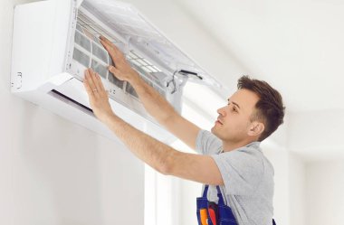 Üniformalı profesyonel elektrikçi modern klimayı içeride mi temizliyor yoksa bakımlı mı? Odadaki erkek teknisyen yeni daireye klima tamir ediyor ya da kuruyor.