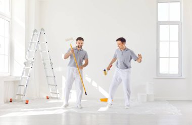 İki adam, ressamlar, bir evin ya da dairenin tadilatı sırasında mutlu bir şekilde dans ediyorlar. Ev yenileme, mutluluk ve takım çalışmasında birlikte çalışan bir takımın neşesi ve yoldaşlığı.