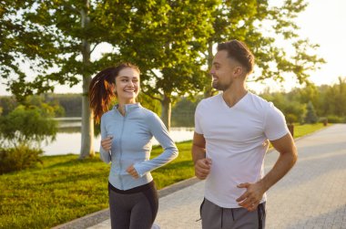 Mutlu sportif dost canlısı insanlar aktif olarak dışarı koşuyor, sağlıklı görünümlü çift koşuyor forma egzersizlerinin tadını çıkarıyor, spor giyim kuşamlarıyla yaz sporları yapıyor, yürüyüş yolu boyunca ilerliyorlar. 