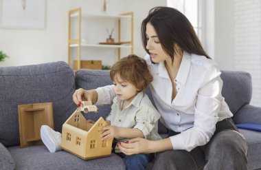 Anne, bebek bakıcısı, küçük çocuk oyuncak evle oynuyor, eğlenceli bir oyun oynuyor, ilgili anne çocuğa öğretmenlik yapıyor, evde eğitici aktivitelerle meşgul, öğreniyor, eğlendiriyor.