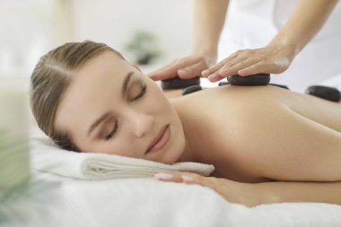 Terapist, spa salonundaki kadın hastalara taş masajı seansı düzenliyor, sağlık ve sağlık konularında uzman bir ortamda rahatlama için lüks bir tedavi üzerinde çalışıyor..