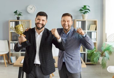 Mutlu, gülümseyen genç bir şirket çalışanının portresi. Makamdaki başarıları için elinde ödül kupasıyla kameraya bakıyor. Genç iş adamları ödül alıyor.