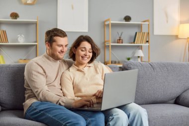 Aile, ilişki ve teknoloji kavramı. Çift dizüstü bilgisayarla, film izleyerek ya da sosyal ağlarda fotoğraf paylaşarak ev sörfü yaparak boş zaman geçirmeyi seviyor. Rahat bir kanepeye oturun.