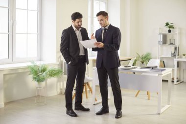 İş yerinin yanındaki ofiste mali belgelere bakan kendine güvenen iki iş adamının portresi. Resmi kıyafet giymiş iş arkadaşları yeni projeler üzerinde konuşuyorlar..