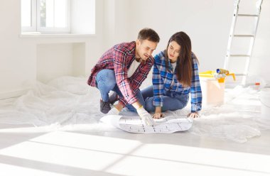 Mutlu gülümseyen genç bir çift apartman planına bakıyor, yeni ev iç tasarımı planlıyor, ev sahipleri tamirattan, boya fikirlerinden, ev mimari planından, taşınmadan bahsediyor. 