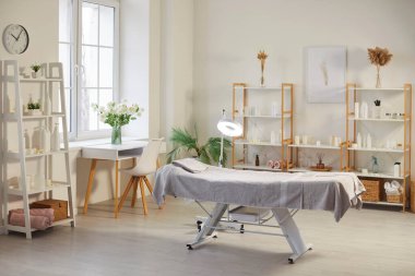 Ortasında güzellik ve cilt ürünleri olan raflarla çevrili masaj masası olan modern, boş bir spa salonu. Yüz ve vücut tedavileri için hazırlanmış güzellik prosedürleri kozmetoloji odası.