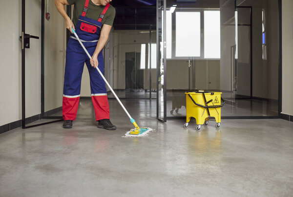 Cropped shot of janitor cleaning floor with mop inside modern commercial building. Cleaning crew member in uniform maintaining cleanliness and hygiene in office space. Routine cleaning service.