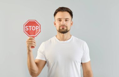 Gri bir stüdyo arka planında elinde kırmızı dur tabelası tutan beyaz tişörtlü genç bir adamın portresi. Uyarı, yasaklama ve kısıtlama kavramı