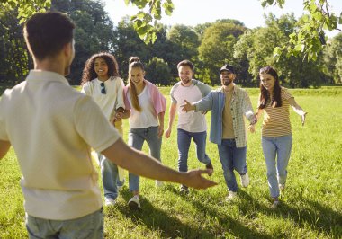 Arkada duran adam yaz parkında dostlarını selamlarken kollarını açtı. Bir grup genç insan birbirlerini kucaklıyor ve doğada birlikte eğleniyorlar. Arkadaşlık kavramı.