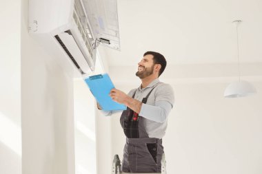 Mutlu işçi tamircisi kontrol ediyor, duvar havalandırma ünitesi yerleştiriyor, havalandırma tamiri, oda sıcaklığı kontrolü, optimal cihaz performansı ayarlanıyor, profesyonel teknisyen iklim sunuyor.