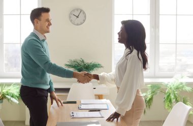 İki mutlu gülümseyen adam ve kadın ofiste el sıkışıyor başarıyı kutluyor, iyi bir anlaşma yapıyor, iş başarısı, sözleşme imzalıyor ya da yeni bir çalışanı iş yerinde selamlıyor..