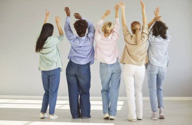 Arka planda, arka planda elleri havada, gri duvarda duran, gündelik giysiler giyen bir grup farklı kadın arkadaşının tam boy portresi var. Çeşitlilik, insanlar ve arkadaşlık kavramı.