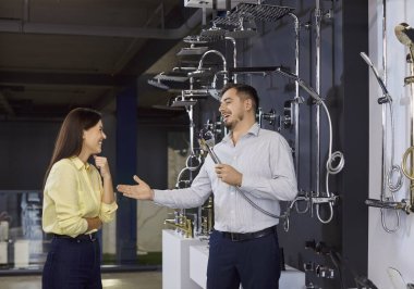 Neşeli satıcı kadın müşteriyle konuşurken eğleniyor, duş başlığı tutuyor, ev tesisatı ürünlerini tavsiye ediyor, müşteriye ev için mükemmel bir ortam sağlıyor..