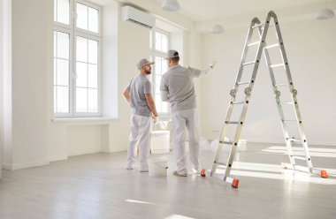 Boyacılar duvar boyası rengini planlıyorlar, merdivenin yanında profesyonel inşaat işçileri koruyucu üniforma giyiyorlar hazırlanmaya hazırlar, oda tamiri işlerini bitiriyorlar, iç mimari işleri yapıyorlar.