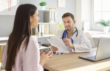 Tıbbi muayene sırasında klinikteki masada oturan dost canlısı erkek doktoru ziyaret eden genç bir kadının portresi. Kadın hasta, ofisteki doktorla konuşuyor. Sağlık ve Tıp Konsepti.