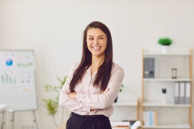 Modern ofiste kollarını kavuşturmuş kameraya bakarken güler yüzlü, güler yüzlü genç bayan şirket çalışanının portresi. İş portresi kavramı.
