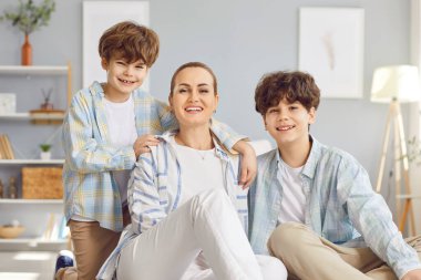 Mutlu aile anne ve iki oğulun portresi. Oturma odasında kucaklaşıp, kameraya bakıp gülümsüyorlar. Sevgi dolu anne hafta sonları çocuklarıyla vakit geçiriyor..