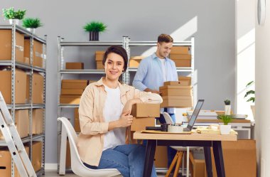 Kadın yönetici elinde karton kutularla lojistik ya da dağıtım merkezinde çalışan erkek meslektaşıyla depodaki depoda müşteri siparişi hazırlıyor. Envanter ve teslimat konsepti.