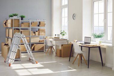 Interior of empty work space with office desk in warehouse with shelves filled cardboard boxes of retail products. Business workplace used for shipping merchandise and stock inventory.