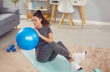 Spor giyimli, sıska, güzel, spor kıyafetli genç bir kadın, sabah sporu yapan bir kız, evde kişisel bayan antrenör, spor salonu, kanepe sağlıklı aktif yaşam tarzı, apartman dairesinde beden eğitimi.