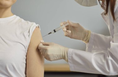 Hasta koluna enjeksiyon, steril eldiven ve beyaz önlük giyen tıbbi uzman, elinde şırınga, rutin tıbbi prosedür, aşı, bakım ve sağlık bakımı klinik odasında. 