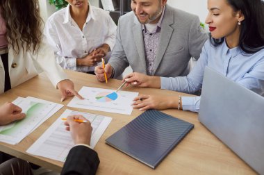 Ofisteki masanın etrafında çeşitli profesyoneller grubu, belgeleri, çizelgeleri, tartışmaları, aktif olarak işbirliği, odaklanmış takım çalışması ve analizleri, iş toplantıları veri yorumlaması ve planlama