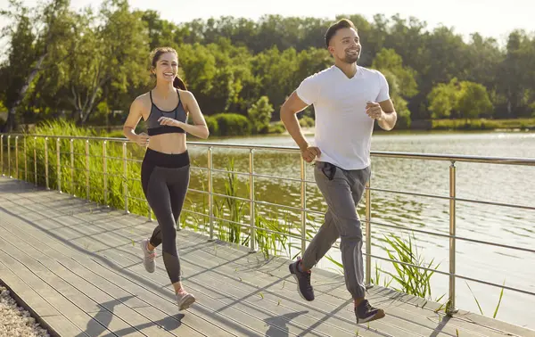 Köprü boyunca birlikte koşan sporcu erkek ve kadın açık havada spor koşusu yapıyorlar. Genç mutlu çift şehir parkında doğa koşusu eğitimi alıyor. Sağlıklı yaşam tarzı ve uygunluk kavramı.
