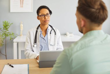 Genç hasta, muayene sırasında klinikteki kadın Afrikalı Amerikalı doktorla konuşuyor. Kadın hekim hastaları dinliyor. Sağlık ve Tıp Konsepti.