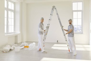 Ressamlardan oluşan gülümseyen mutlu bir takımın portresi ellerinde boya ruloları olan kameralara bakıyor ve yeni dairenin duvarını boyamaya gidiyor. İnşaat müteahhitleri tadilat yapıyor. Onarım servisi kavramı.