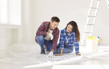 Yeni dairenin planlarıyla yerde oturan mutlu genç çift evlerinin tasarım projesini tartışıyor. Kadın ve erkek yeni bir dairede tamirat yapmayı planlıyor. Yenileme ve taşınma konsepti.