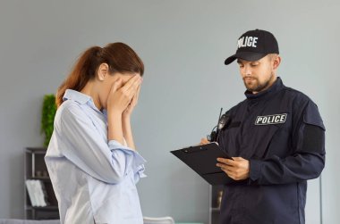 Bir polis memuru ev ziyareti sırasında not alırken genç bir kadın yüzünü sıkıntıya sokuyor. Olay yeri, kolluk kuvvetleri desteği, duygusal travma ve mağdur yardımını yansıtıyor.. 