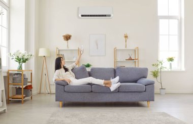 Kafkas genç bayan rahat koltukta dinleniyor, uzaktan kumandayla klimayı açıyor, soğutma ya da ısıtma sistemini açıyor, modern oturma odasındaki rahat sıcaklığı ayarlıyor.