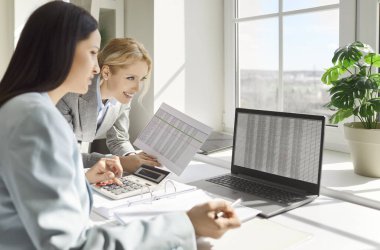 Ofiste çalışan iki neşeli, gülümseyen bayan iş adamı iş yerinde dizüstü bilgisayarlarıyla şirketin mali durumunu analiz eden bilgisayar monitörüne bakıyorlar. Muhasebeci iş konsepti.