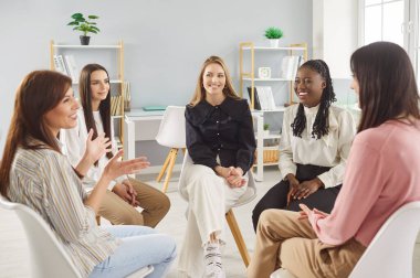 Çeşitli kadınlar konuşma çemberi kuruyor, mutlu destekleyici terapi grubu tartışmaları, konuşma, el kol hareketi, dinleme ilgi ve anlayış içinde gülümseme, iletişim kulübü ve paylaşılan deneyimler