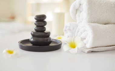 Spa seti, rulo havlular, tepside sıcak taşlar, Asyalı çiçek sükuneti düzenleme, rahatlama ve sağIık, terapi sükuneti, klinikte bekleyen barışçıl spa deneyimi atmosferi.