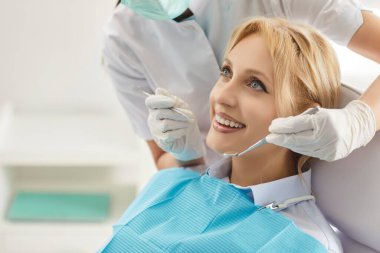 Mutlu kadın dişçi kliniğine gidiyor, diş kontrolü için dişçiye gidiyor, dişleri bile beyaz. Tanımlanamayan diş doktoru profesyonel aletler kullanıyor, diş prosedürü uyguluyor.