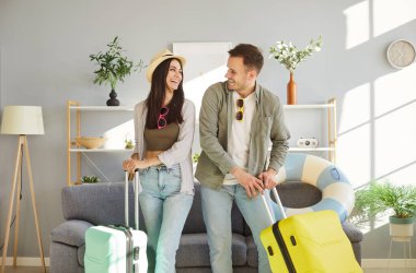 Mutlu, genç, gülümseyen bir çiftin portresi. Evdeki oturma odasında bavullarıyla tatil gezisi için hazırlar. Neşeli adam ve kadın yaz tatiline gidiyor. Seyahat ve seyahat kavramı.