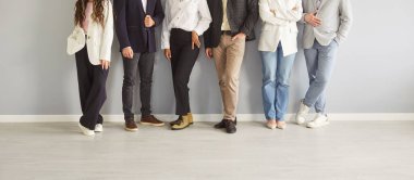 Tanımlanamayan iş adamlarının bacakları büroda gri bir duvarın yanında sıraya girmiş. Tarz sahibi bir grup çalışanın ya da günlük kıyafetlerle çekilmiş bir fotoğrafı. Pankart.