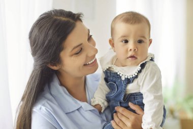 Sevgisini ifade eden, gülümseyen ve evde poz veren esmer, genç bir anne. Hassas an, aile ve bağ kurma konsepti. Çocuklar büyütür.