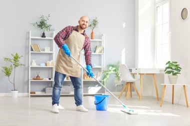 Kameraya gülümseyen bir adamın portresi elinde paspasla ev ya da ofis paspası tutuyor. Erkek temizleyici, yerleri yıkıyor. Ev işi, temizlik hizmeti ve temizlik konsepti.