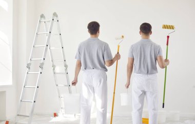 Üniformalı iki erkek ressam duvara bakar, arkasını görür. Beyaza boyamayı bitirdim. Müteahhitlerin profesyonel işi. Dairede yeni bir iç mekan. Kovalarca boyası olan işçiler, yakın plan.