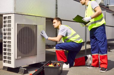 Erkek mühendisler çatıdaki havalandırma veya havalandırma sistemini onarmak veya onarmak için iş birliği yaparlar. Uzman servisleri, hava kontrol sisteminin optimum işlevselliğini sağlar.